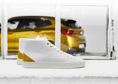 Image from x2sneaker.bmw website showing BMW x2 Sneaker on a windowsill with gold BMW x2 vehicle in the background.