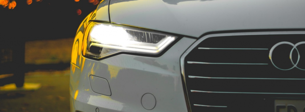 front of white Audi vehicle showing headlights and half of Audi badge