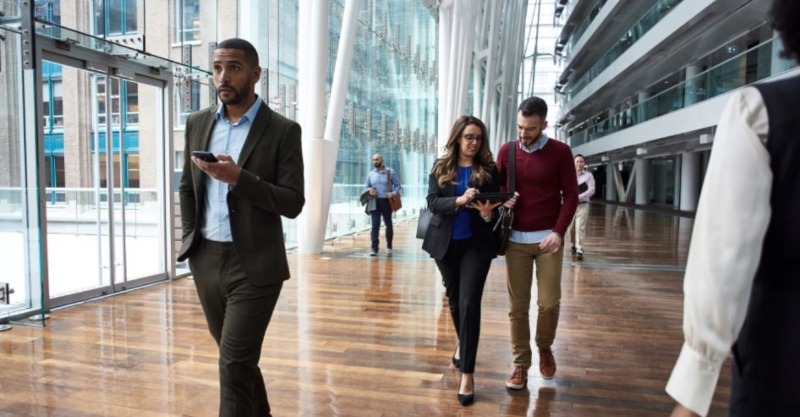 people walk through office hallway reading from mobile phones microsoft 365