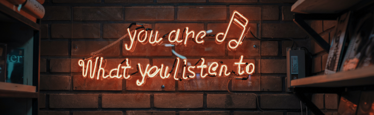 Neon writing on a brick wall reads, "you are what you listen to" with records on shelves