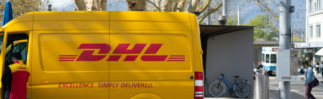 DHL delivery van parked with delivery man standing outside the van with open door.